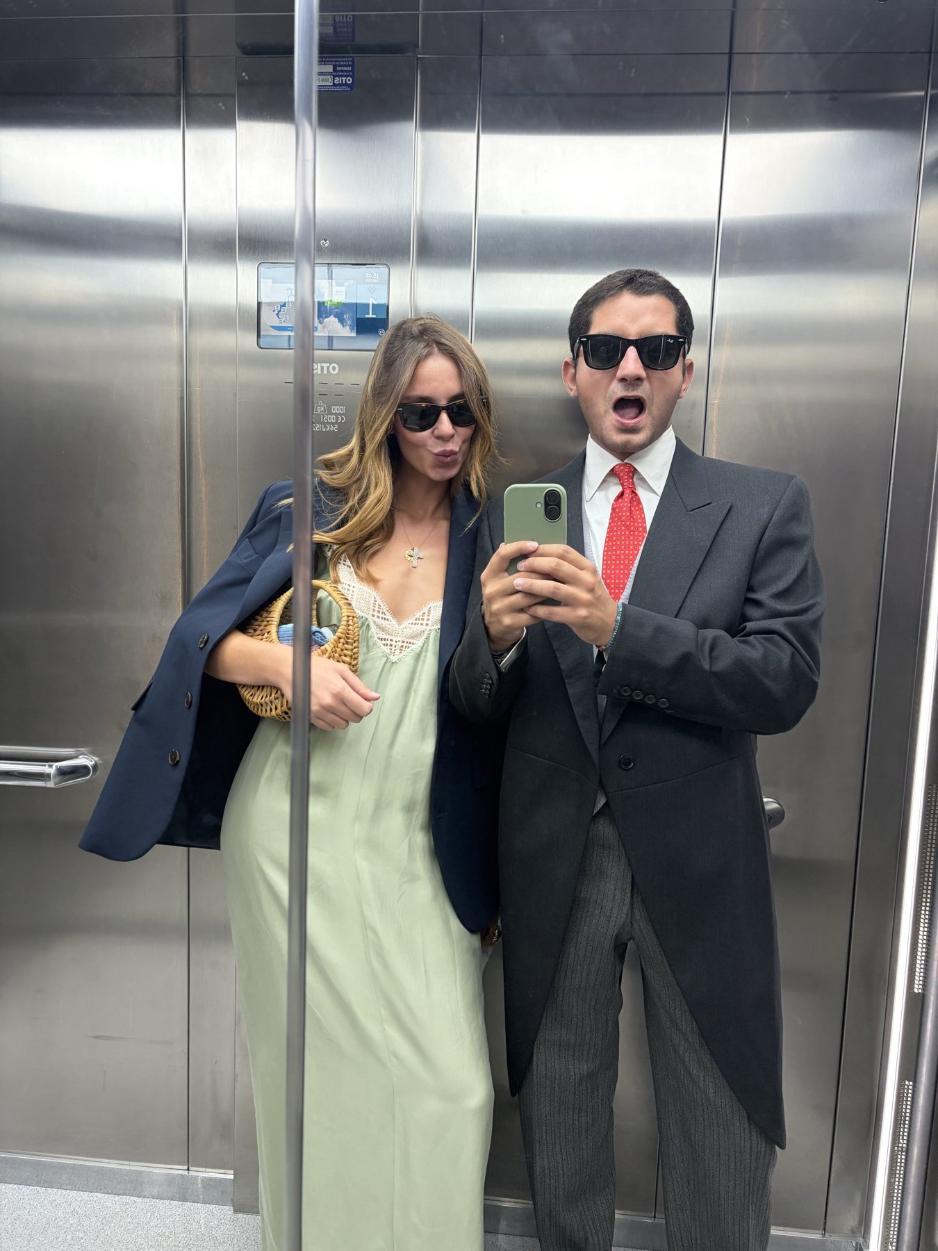 Jacopo in a morning coat and sunglasses, taking a lift mirror selfie with a companion